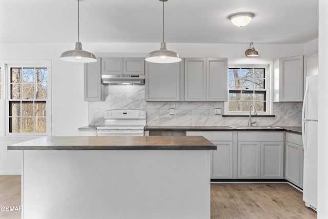 kitchen featuring light wood-style flooring, under cabinet range hood, white appliances, a sink, and decorative backsplash