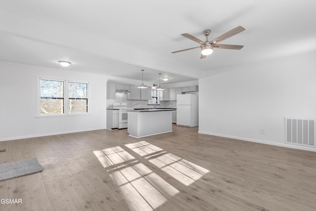 unfurnished living room with baseboards, visible vents, ceiling fan, and light wood finished floors