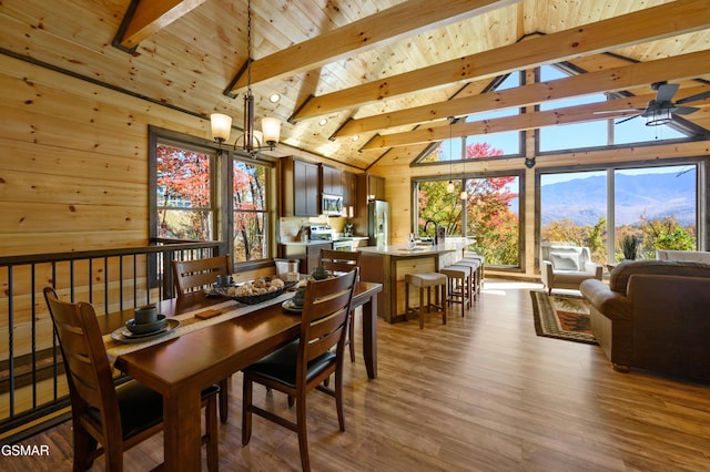 dining space with wood ceiling, ceiling fan with notable chandelier, beamed ceiling, a mountain view, and light hardwood / wood-style floors