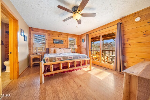 bedroom with access to exterior, wooden walls, a textured ceiling, and light wood-type flooring