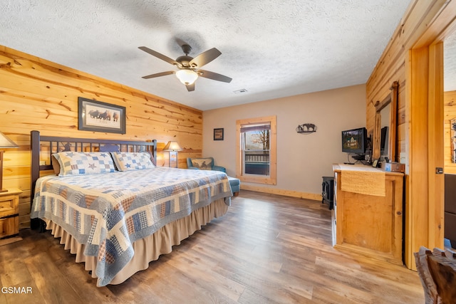 bedroom featuring ceiling fan, wood-type flooring, wooden walls, and a textured ceiling