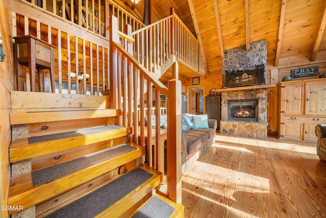 stairs with a stone fireplace, hardwood / wood-style floors, wood walls, beamed ceiling, and wood ceiling