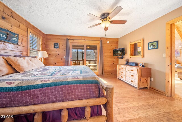 bedroom featuring wooden walls, access to exterior, ceiling fan, light hardwood / wood-style floors, and a textured ceiling