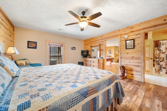 bedroom featuring ceiling fan, light hardwood / wood-style floors, a textured ceiling, and wood walls