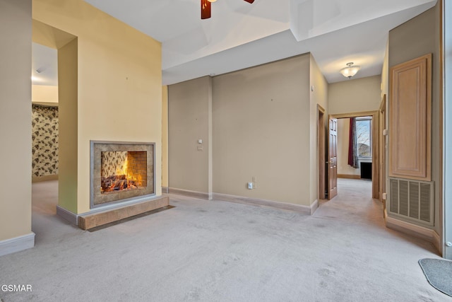 unfurnished living room with a lit fireplace, visible vents, light carpet, and baseboards