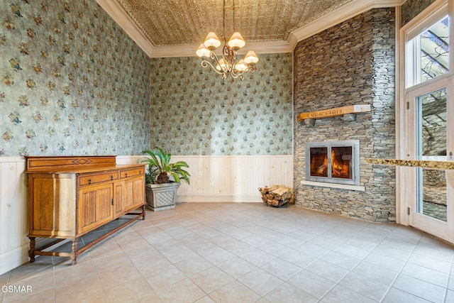 interior space featuring wallpapered walls, wainscoting, ornamental molding, a stone fireplace, and a notable chandelier