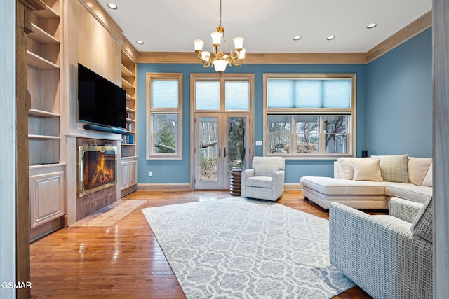 living area with built in features, baseboards, light wood-style flooring, a fireplace with flush hearth, and an inviting chandelier