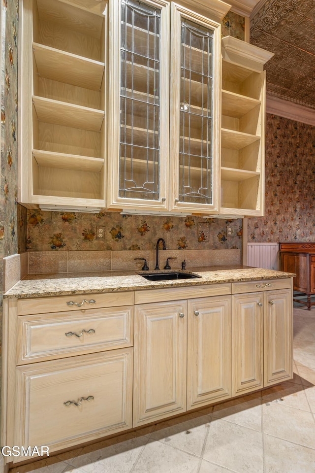 kitchen featuring wallpapered walls, light stone counters, cream cabinets, open shelves, and a sink