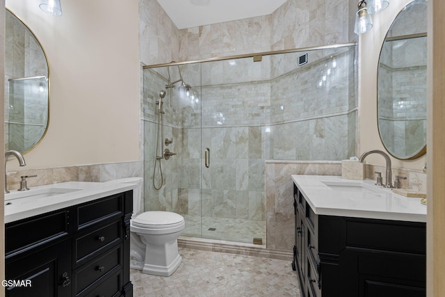 full bath featuring a stall shower, two vanities, a sink, and tile walls