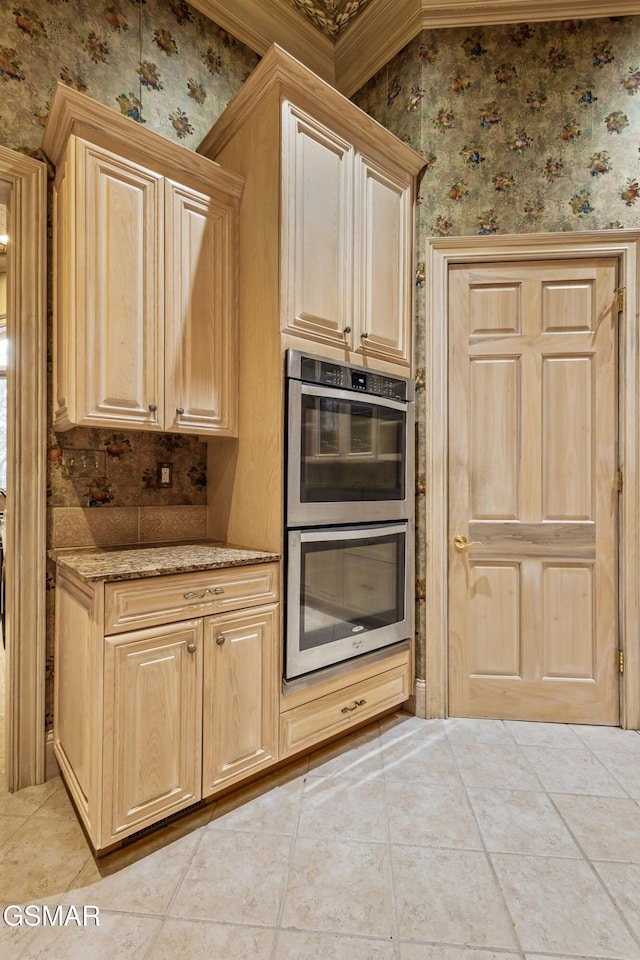 kitchen featuring stainless steel double oven, light tile patterned flooring, light brown cabinets, light stone countertops, and wallpapered walls