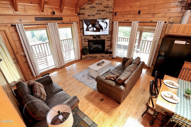 living room with vaulted ceiling with beams, a stone fireplace, light wood-style flooring, and wooden walls