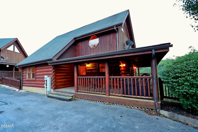 cabin with covered porch, a shingled roof, and log siding