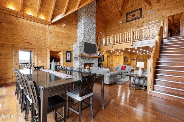 dining room with wood ceiling, high vaulted ceiling, wood-type flooring, a stone fireplace, and beamed ceiling