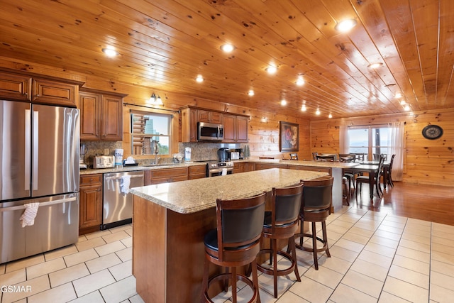 kitchen with a kitchen island, appliances with stainless steel finishes, wooden ceiling, and a kitchen bar