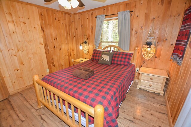 bedroom with ceiling fan, wood walls, and wood-type flooring