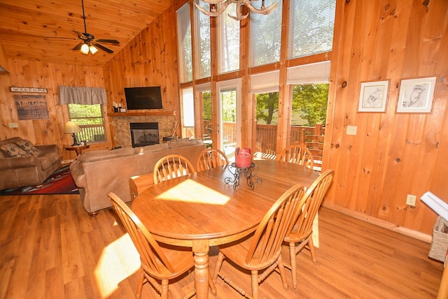 dining room featuring high vaulted ceiling, ceiling fan, a fireplace, light hardwood / wood-style floors, and wood ceiling