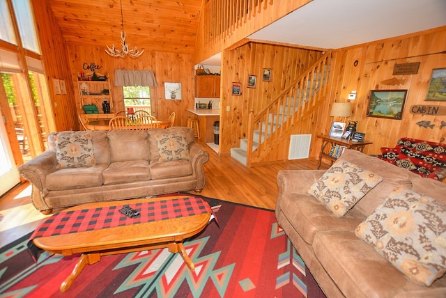 living room featuring wood walls, wood-type flooring, lofted ceiling, and an inviting chandelier