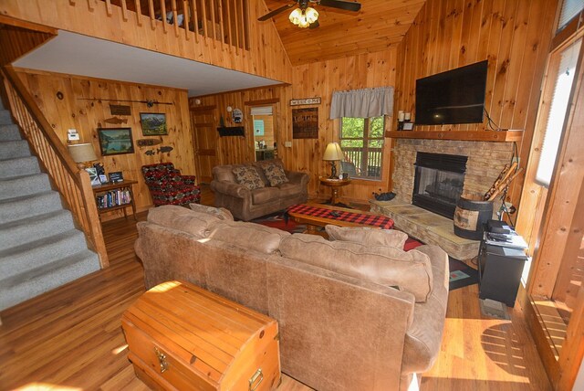 living room with ceiling fan, wooden ceiling, wood walls, light hardwood / wood-style floors, and a fireplace