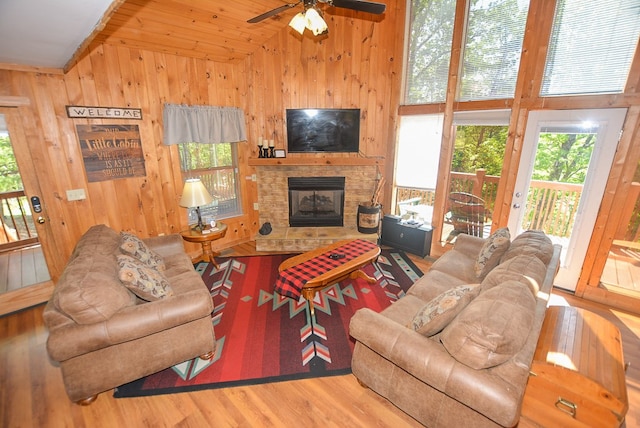 living room with ceiling fan, a stone fireplace, wood-type flooring, and high vaulted ceiling