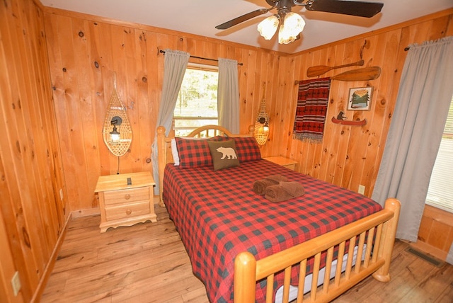 bedroom with light wood-type flooring, ceiling fan, and wood walls