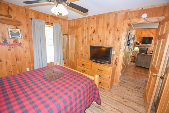 bedroom with ceiling fan, a stone fireplace, wooden walls, and light hardwood / wood-style flooring