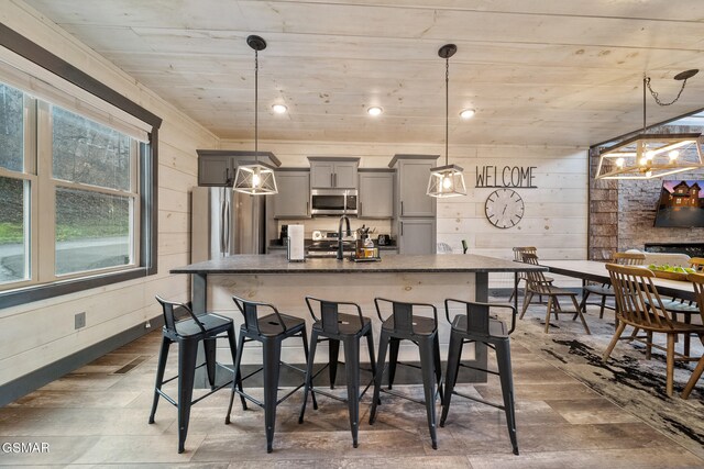 1125 Autumn Path Way, Sevierville, TN 37862 - kitchen featuring gray cabinetry, stainless steel appliances, decorative light fixtures, a kitchen bar, and wooden walls