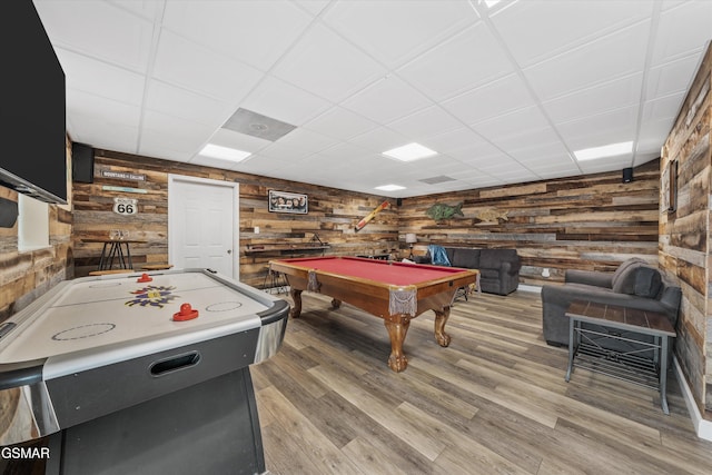 recreation room featuring wooden walls, a drop ceiling, and light wood finished floors