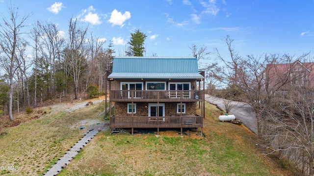 back of house featuring a lawn, driveway, metal roof, and a deck