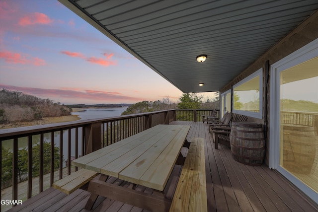 deck at dusk with outdoor dining area and a water view