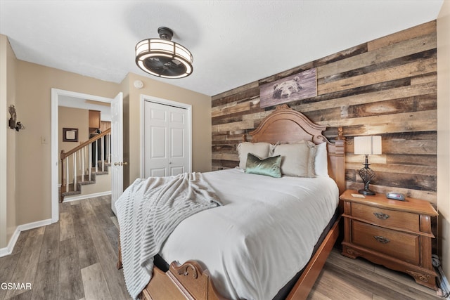 bedroom featuring wooden walls, wood finished floors, a closet, and baseboards