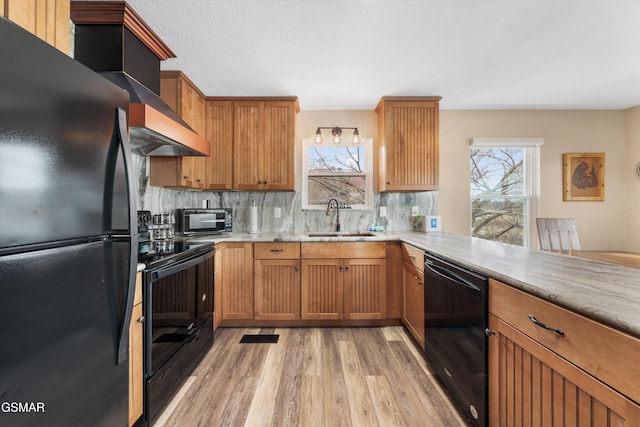 kitchen with light wood finished floors, light stone countertops, decorative backsplash, black appliances, and a sink