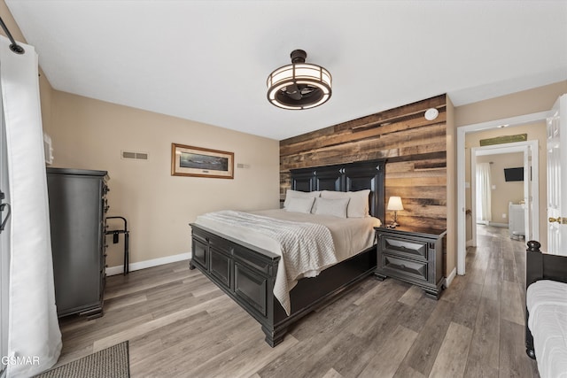 bedroom with light wood finished floors, wooden walls, visible vents, an accent wall, and baseboards