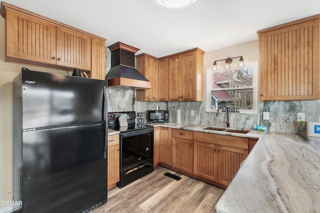 kitchen with backsplash, black appliances, wall chimney range hood, and a sink