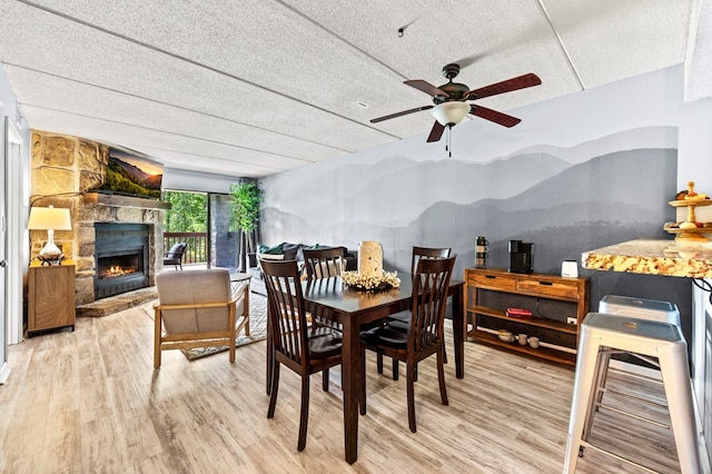 dining space featuring wood-type flooring, a textured ceiling, a stone fireplace, and ceiling fan