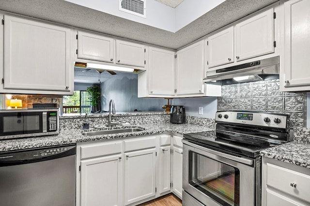 kitchen featuring white cabinets, appliances with stainless steel finishes, light stone countertops, and sink