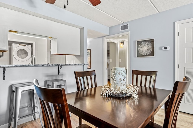 dining space with stacked washer / dryer, ceiling fan, light hardwood / wood-style flooring, and a textured ceiling