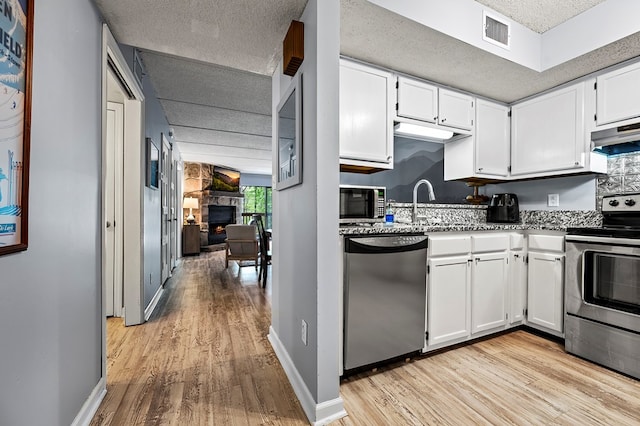 kitchen featuring ventilation hood, stainless steel appliances, light hardwood / wood-style flooring, a fireplace, and white cabinetry