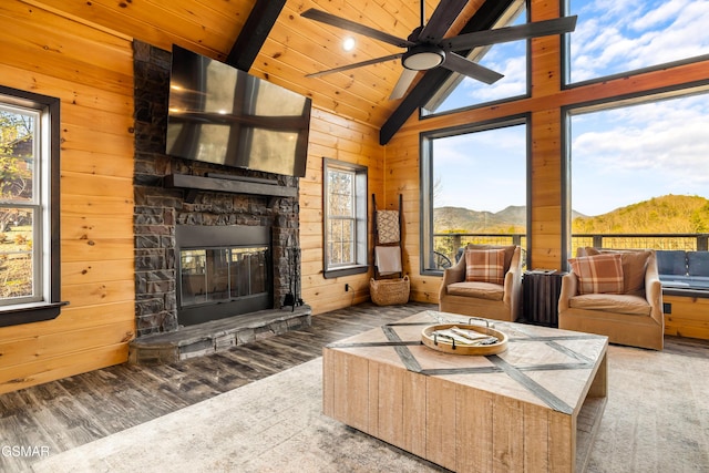 living area featuring wooden walls, plenty of natural light, an outdoor stone fireplace, and wood finished floors