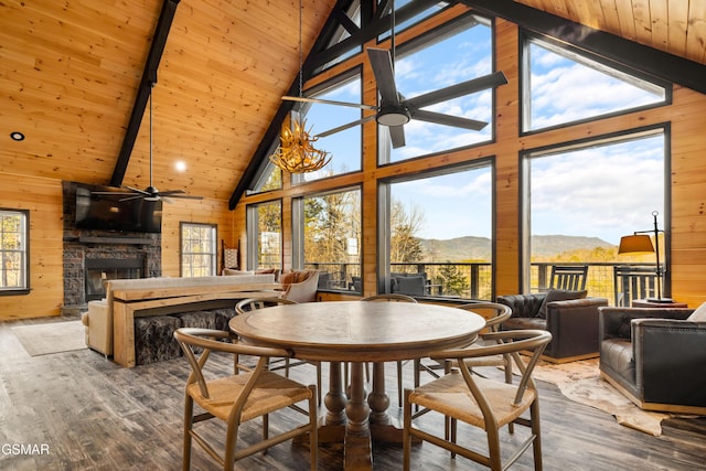 dining room with a mountain view, wooden ceiling, wood walls, a fireplace, and ceiling fan