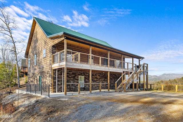 back of house with metal roof, stone siding, and log exterior