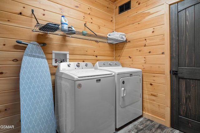 clothes washing area with washer and dryer, laundry area, wooden walls, and dark wood-style floors