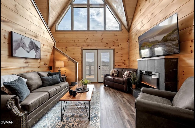 living room with french doors, wooden walls, wood-type flooring, high vaulted ceiling, and a fireplace