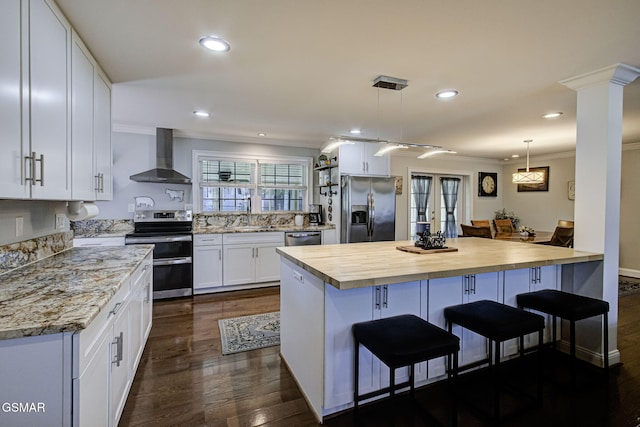 kitchen with a breakfast bar, appliances with stainless steel finishes, white cabinets, wall chimney exhaust hood, and crown molding