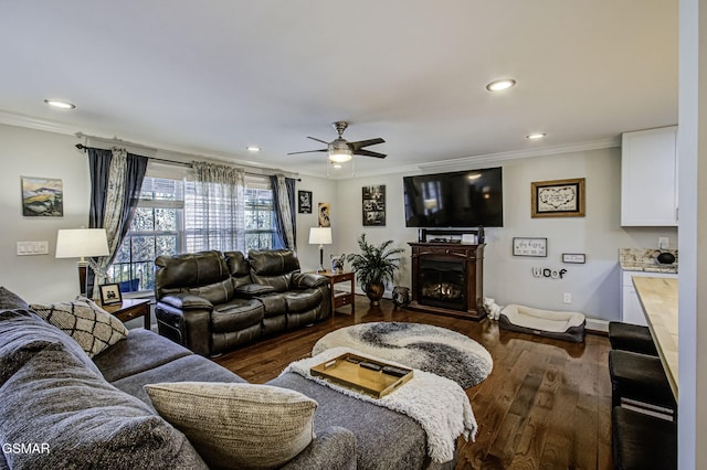 living room with dark wood-style floors, recessed lighting, a warm lit fireplace, and crown molding