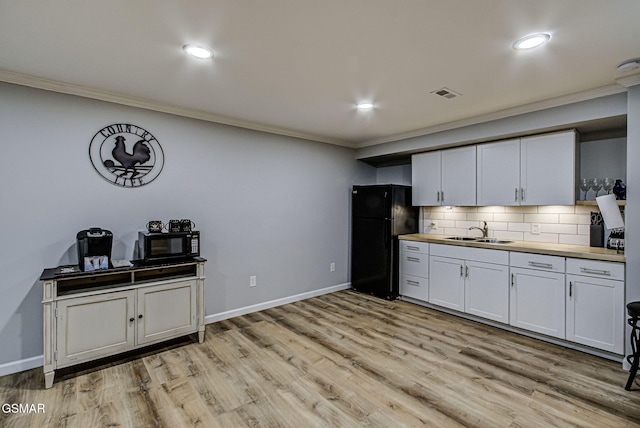 kitchen with visible vents, a sink, backsplash, freestanding refrigerator, and crown molding