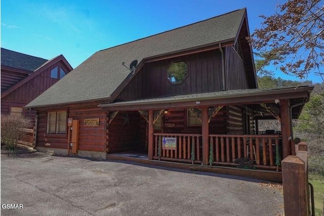 log-style house featuring log exterior, a porch, and roof with shingles