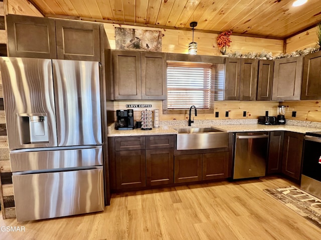 kitchen with pendant lighting, stainless steel appliances, wooden walls, and sink