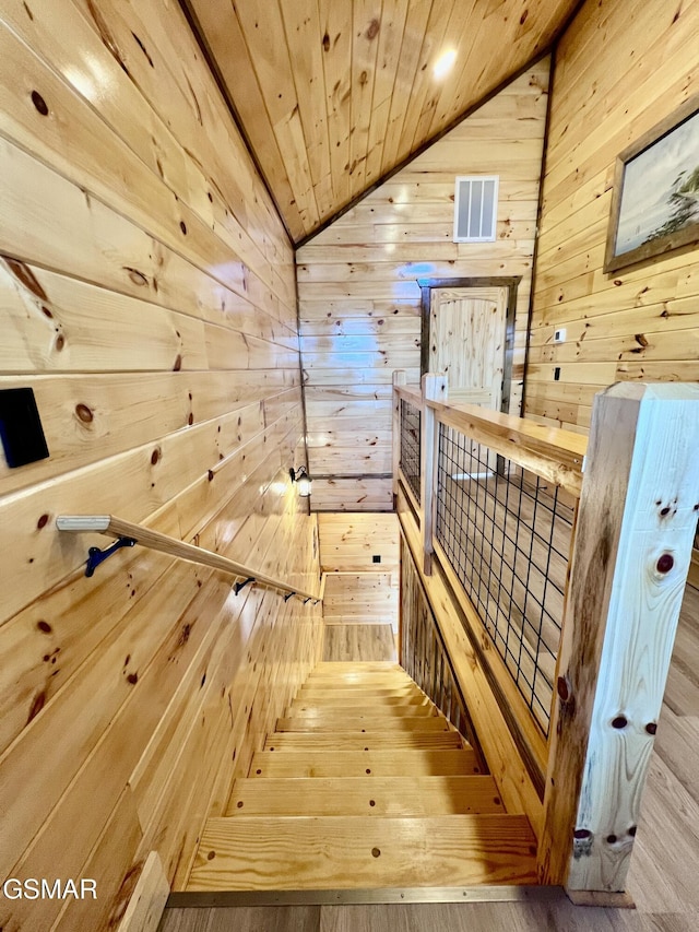 staircase with wood walls, wooden ceiling, vaulted ceiling, and wood-type flooring