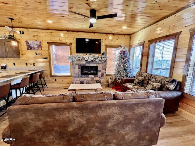 living room featuring wood walls, wooden ceiling, a stone fireplace, light hardwood / wood-style flooring, and ceiling fan