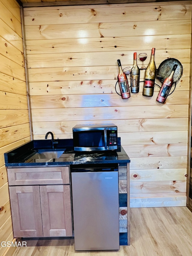 kitchen featuring light wood-type flooring, fridge, wooden walls, and sink